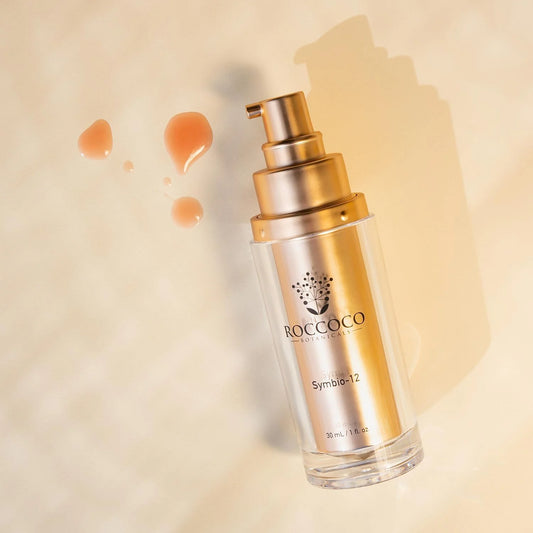 Skincare serum bottle of Symbio-12 with gold pump on a beige background, featuring the brand 'Roccoco'.